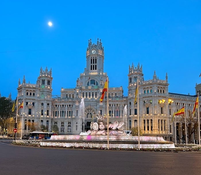 The Cybele Palace is one of the most beautiful buildings in the city centre of Madrid, pictured here with a blue sky and bright moon at night with lights on the fountain