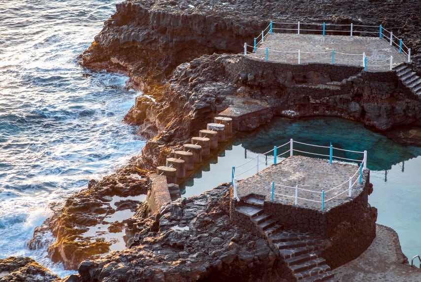 The natural swimming pool of Charco Azul in La Palma, Canary Islands, with its clear blue waters and stone steps leading into the sea, bordered by volcanic rock, is an inviting spot for a refreshing dip and a top choice for free things to do in La Palma.