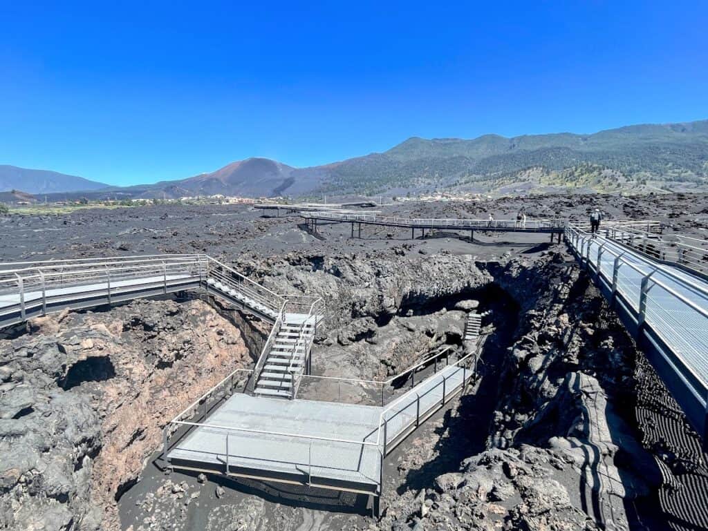 Visitors navigate the metal stairways amidst the black volcanic terrain at Caños de Fuego, near the Cueva de Las Palomas Volcanic Tube in La Palma