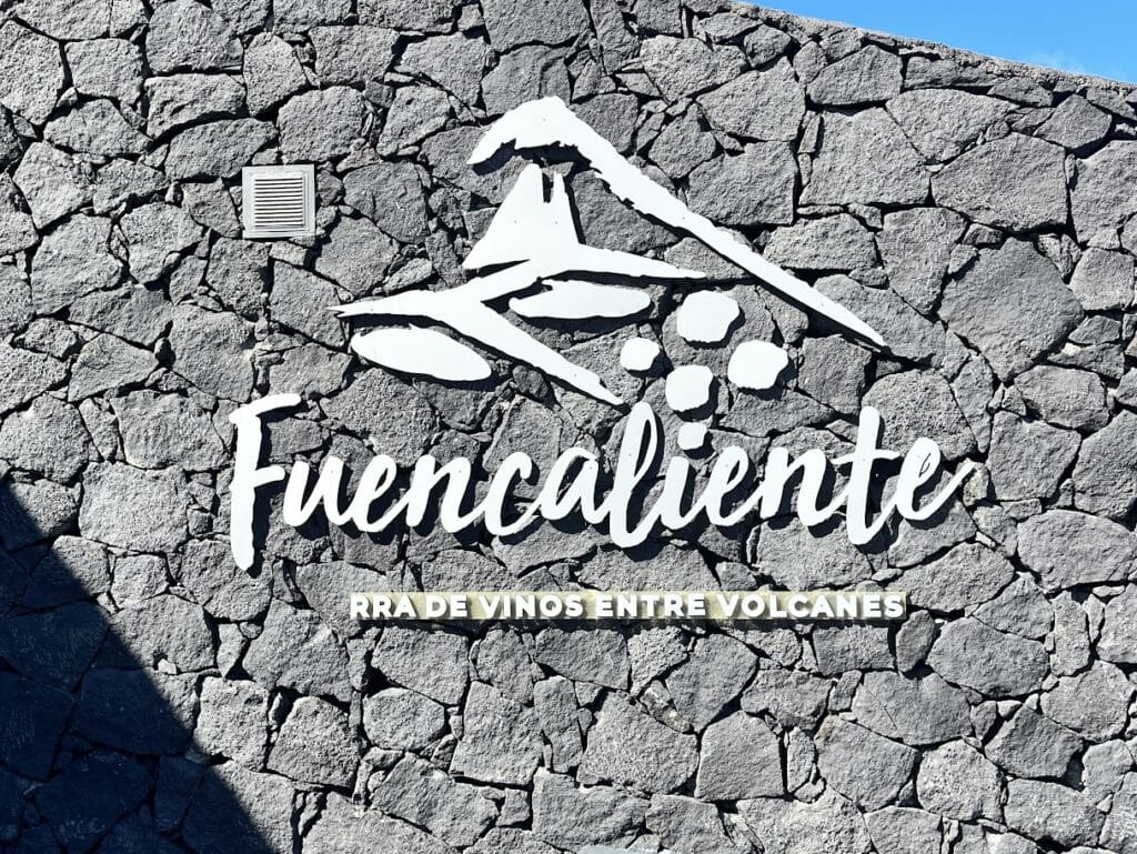 A striking white wall mural of the Fuencaliente La Palma logo, emblazoned on a background of black volcanic rocks, reads "Tierra de vinos entre volcanes".