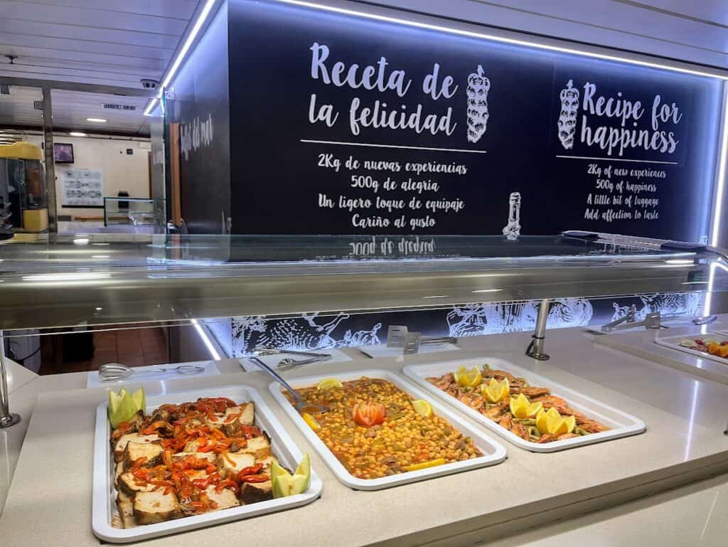 Buffet area on a ferry with various dishes on display, including "Recipe for Happiness" written on the wall – a creative touch for those figuring out how to get to La Palma.