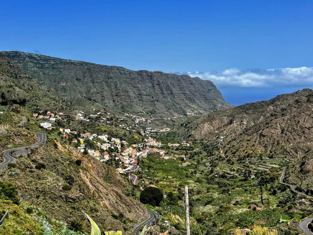 A panoramic view of a Hermigua valley with a meandering road leading through small villages nestled between mountain ranges.