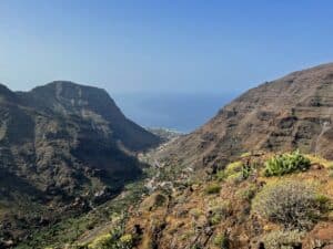 View from a high vantage point at Mirador de la Curva del Queso overlooking the deep, rugged valley of Valle Gran Rey on La Gomera, Canary Islands, with the Atlantic Ocean in the distance, terraced hillsides below, and a clear blue sky above.
