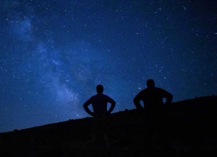 Silhouetted against a starry sky, two people are immersed in the beauty of La Palma's stars, a scene capturing the essence of La Palma stargazing tours.