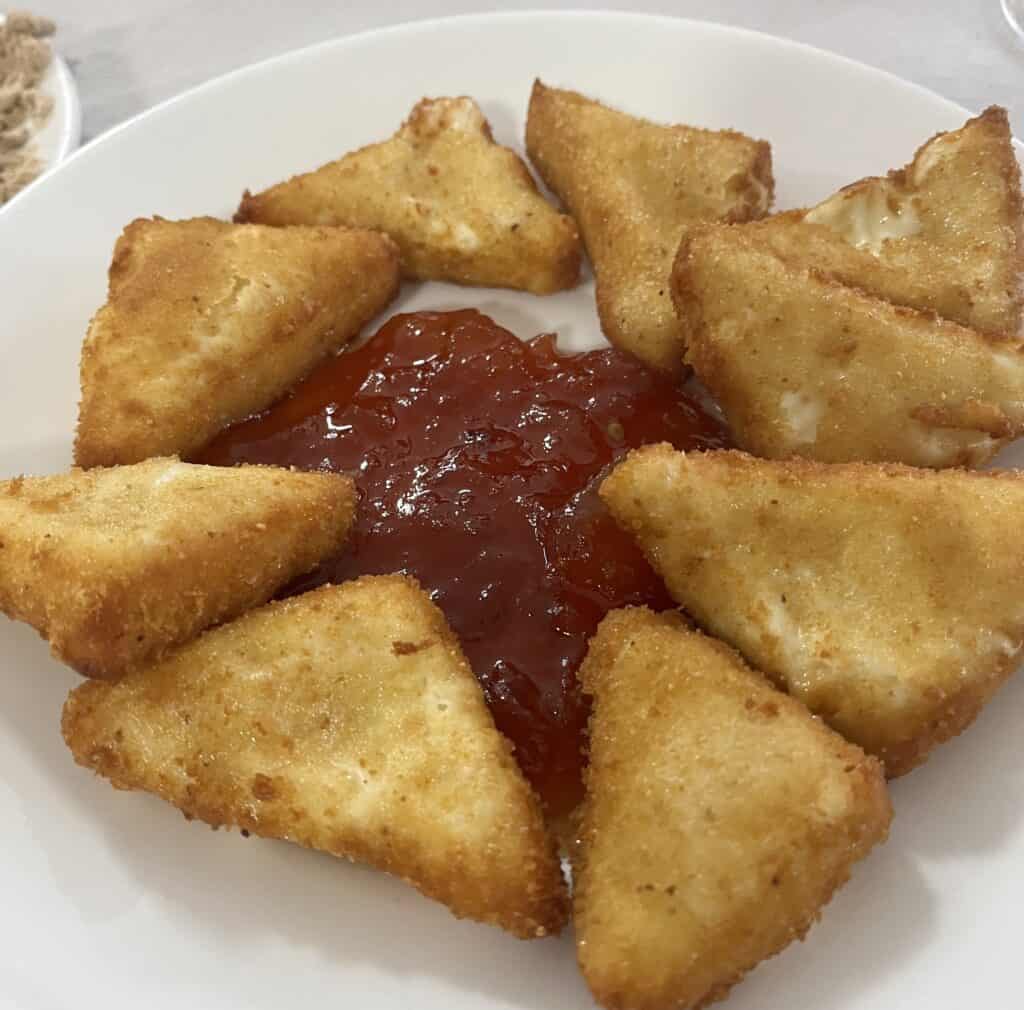 A plate of Queso Palmero, traditional fried cheese triangles from La Palma, served with a red dipping sauce, arranged in a circle on a white plate.