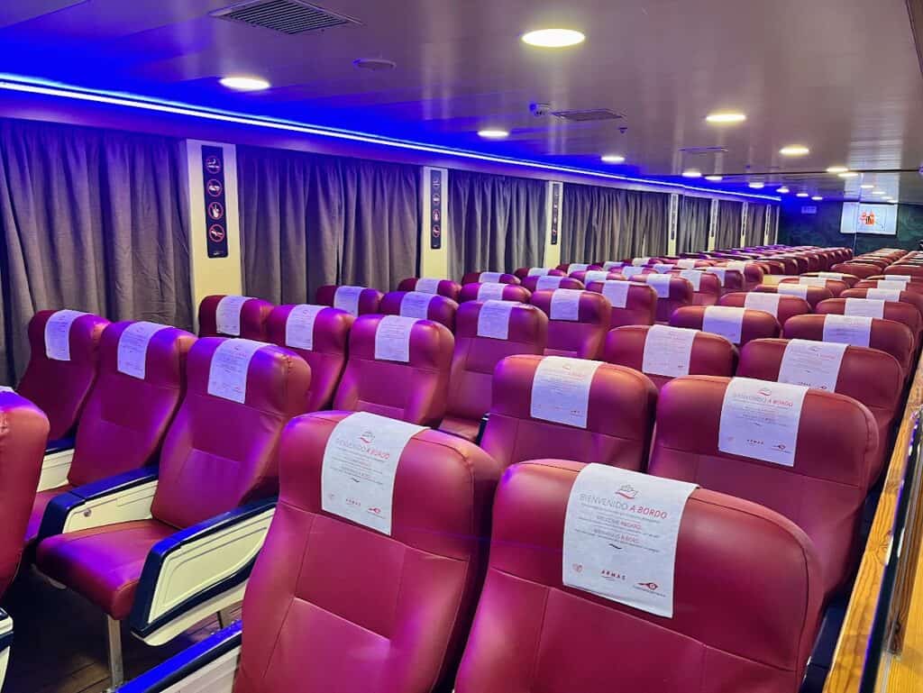 Rows of red seats next to windows with curtains drawn inside a ferry's lounge area – a comfortable spot for travelers on a day trip to La Palma from Tenerife.