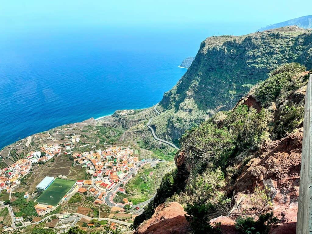 An aerial perspective from Mirador de Abrante in La Gomera, overlooking the verdant valley of Agulo with its patchwork of fields leading down to the azure sea.