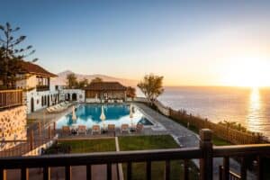 This tranquil sunrise scene over a refreshing swimming pool at Parador de La Gomera invites travelers to consider it as a prime option for where to stay in La Gomera, highlighting the pool's crystal waters, flanked by sun loungers, with a panoramic ocean view and a silhouette of a volcanic peak in the distance.