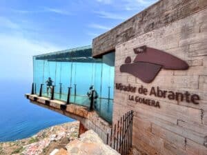 Tourists at Mirador de Abrante in La Gomera taking pictures at the glass observation deck, surrounded by the natural beauty of the island's rugged terrain and the vast ocean.