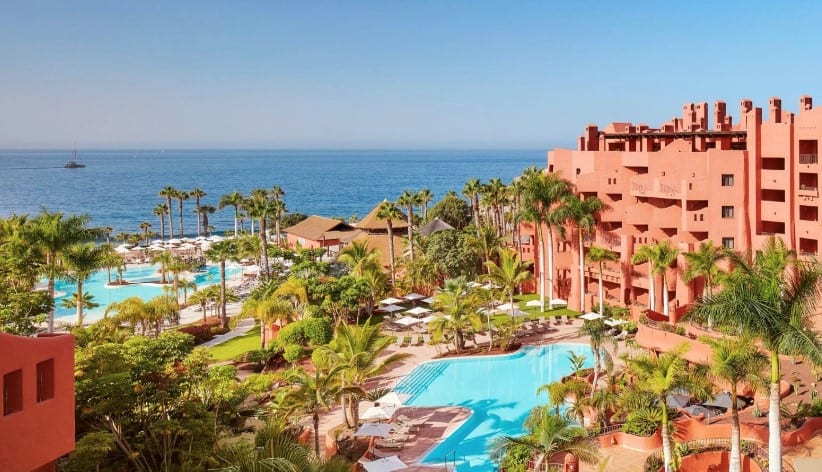 Luxurious poolside view at Tivoli La Caleta Resort, one of the best hotels in Costa Adeje, featuring palm trees and comfortable lounge chairs overlooking the ocean.