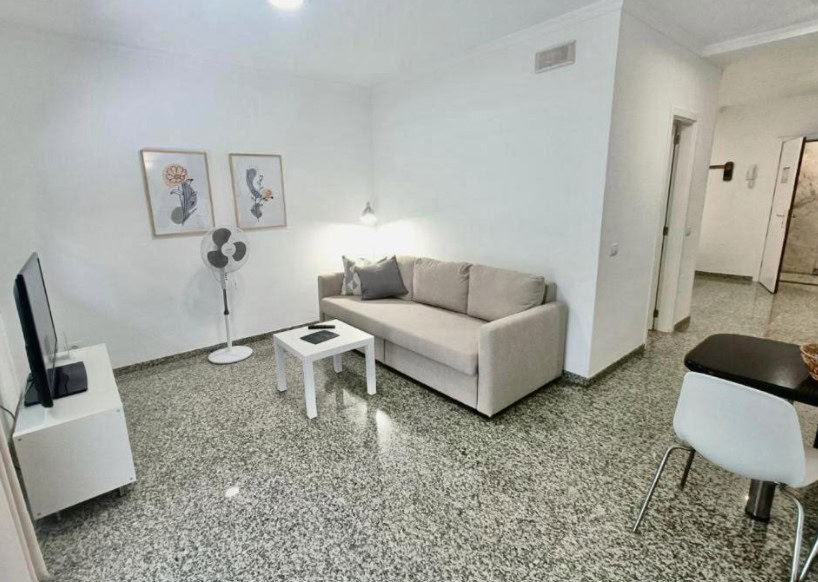 The living room at Apartamentos Sol Mar, one of the best hotels in Los Cristianos, offers a minimalist design with a comfortable sofa and TV.