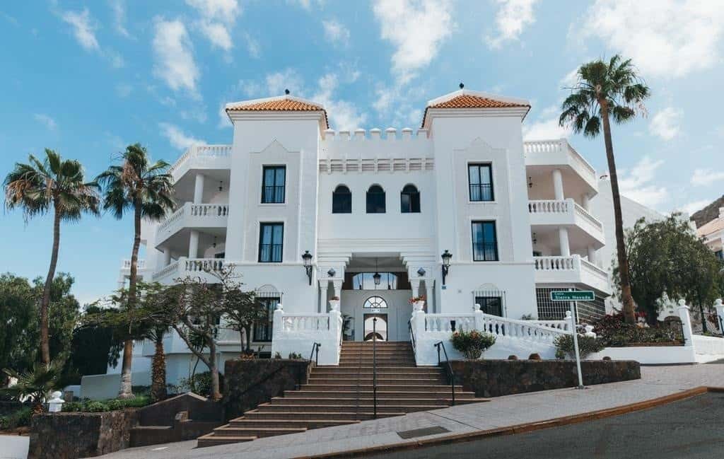 The front of Beverly Hills Heights, one of the best hotels in Los Cristianos, showcases a grand white building with palm trees.