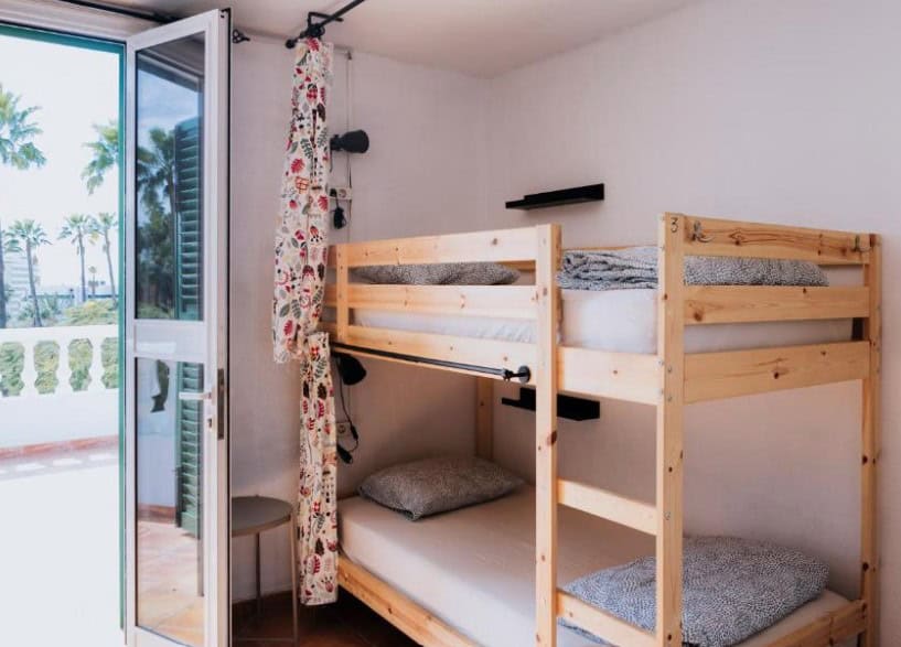 Simple room with wooden bunk beds and a door leading to a balcony at Endless Summer Hostel, one of the cheap hotels in South Tenerife.
