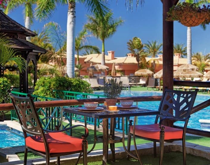 The poolside dining area at Green Garden Eco Resort & Villas, one of the Los Cristianos hotels on the beach, is surrounded by lush palm trees.