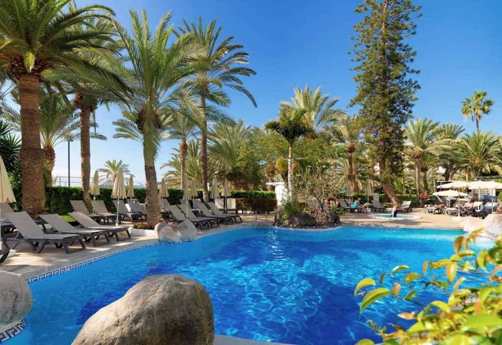The serene pool area at H10 Big Sur, one of the best Los Cristianos hotels on the beach, is lined with sun loungers and palm trees.