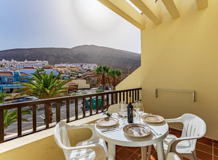 The balcony at Klayman Olivina Aparthotel, one of the best hotels in Los Cristianos, offers a cozy outdoor dining setup with a mountain view.