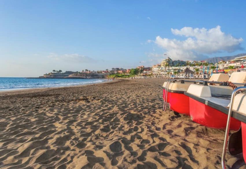 Red boats on the sandy beach with the ocean and hotels in the background at Royal Sunset Beach Club, ideal for the best hotels in South Tenerife for families.