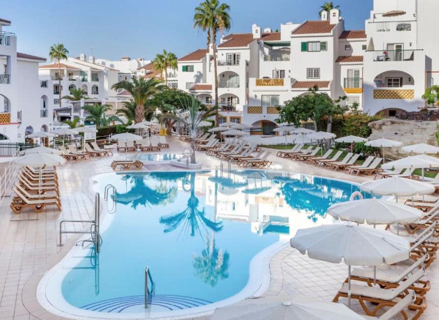 Elegant pool area with sun loungers and white buildings at Sunset Harbour Club, representing Costa Adeje hotels.
