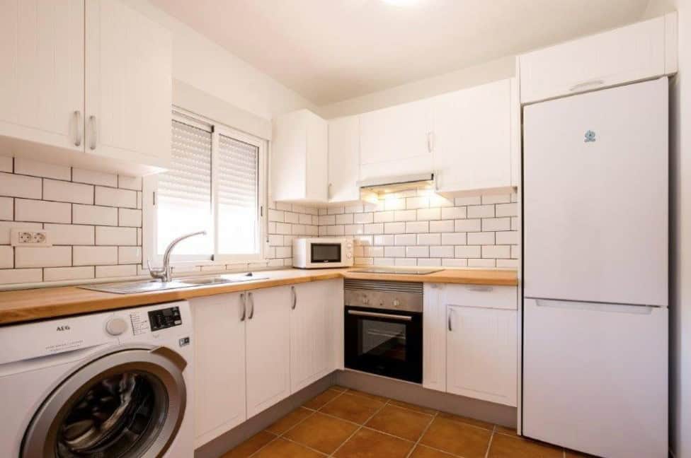 The kitchen at Tantulia Bungalows Tamaragua, one of the cheap hotels in Los Cristianos, features modern appliances and white cabinetry.
