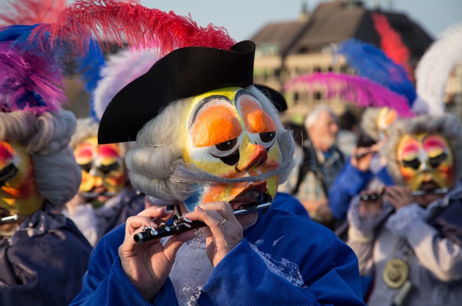 Musicians in vibrant, traditional costumes playing flutes during Basel's Fasnacht Carnival.