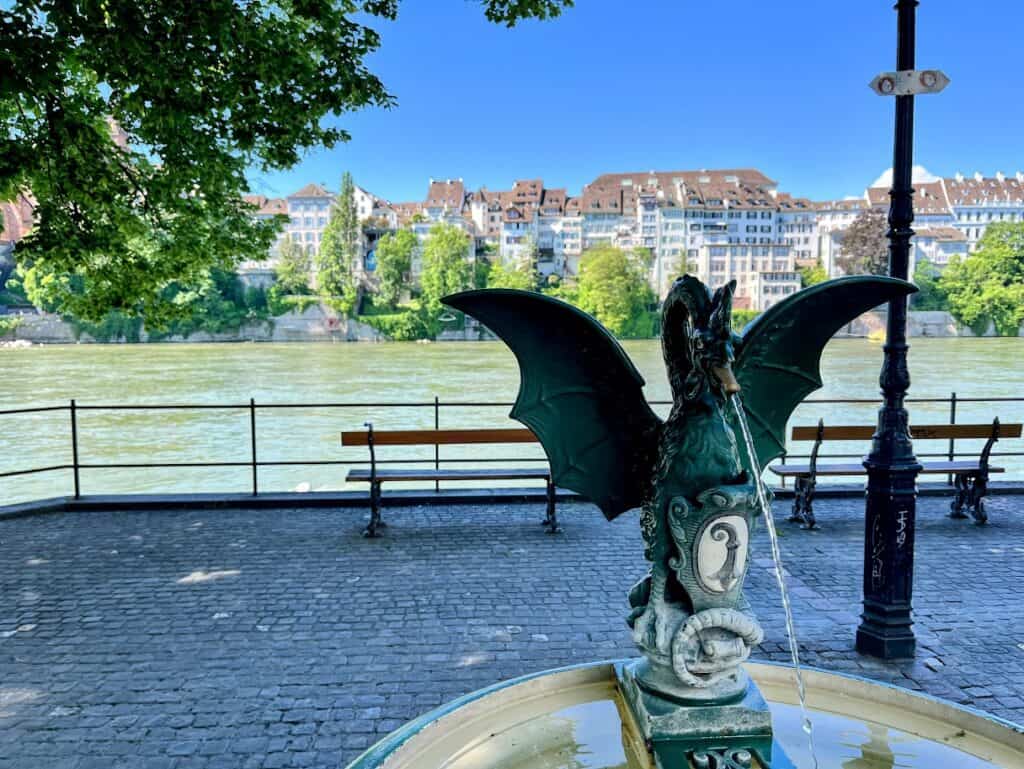 A close-up of the ornate dragon fountain by the Rhine River, with picturesque views of the riverbank. This charming spot is perfect for a stroll and captures the essence of 1 day in Basel.