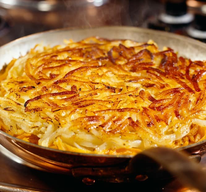 A delicious plate of Rösti, a Swiss specialty made from crispy fried potatoes, presented in a rustic pan and garnished with herbs.