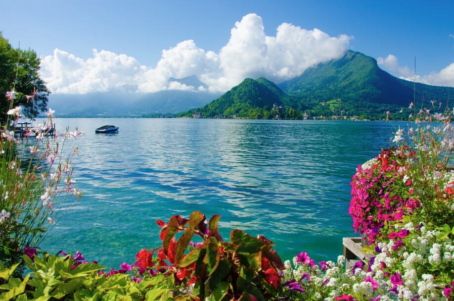 A breathtaking view of Lake Annecy, surrounded by lush green mountains and dotted with boats gliding across its crystal-clear waters. This stunning natural setting is a highlight of any Geneva to Annecy tour, offering opportunities for boating, swimming, and simply enjoying the tranquil beauty of the French Alps.