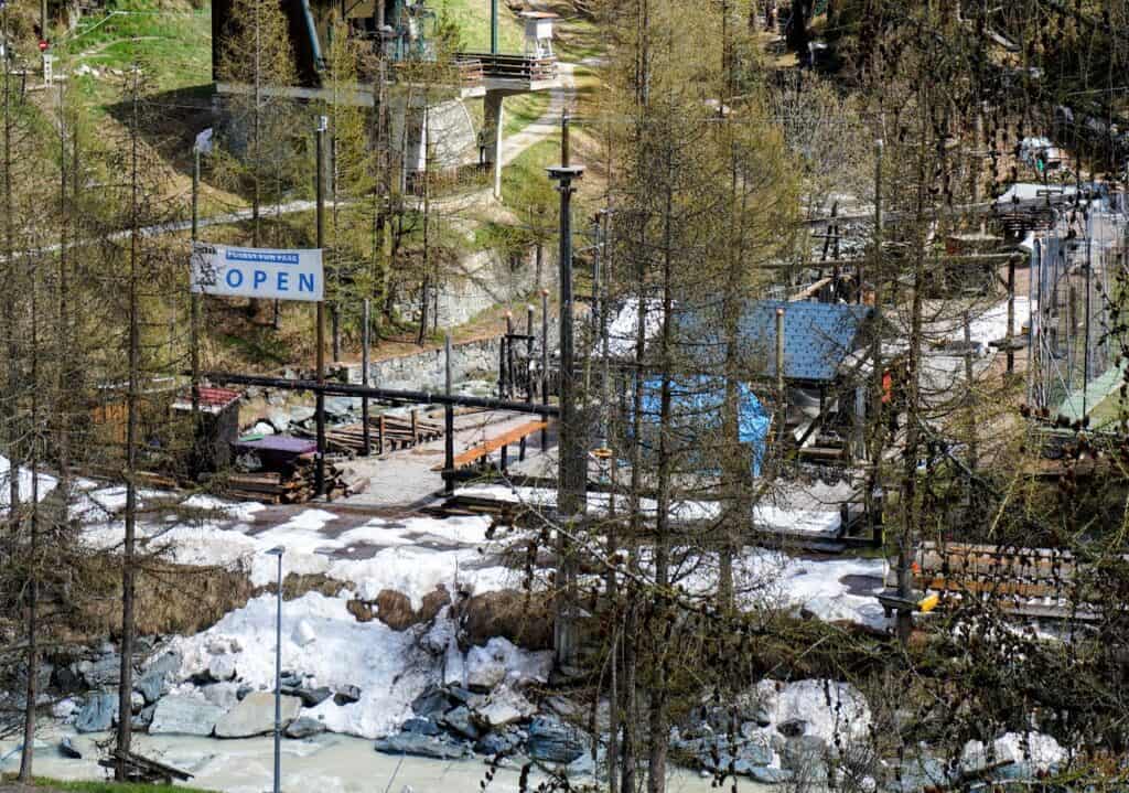 Forest Fun Park Zermatt presents a lively outdoor adventure area featuring ropes courses and zip lines amidst a backdrop of lush trees and vibrant greenery. This exciting venue is perfect for families and friends looking for fun activities during their summer visit.