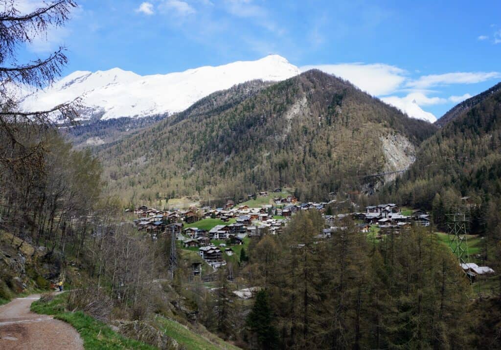 A scenic hiking path above Zermatt, with stunning views of the village below and the snow-covered peaks of the Swiss Alps in the distance.