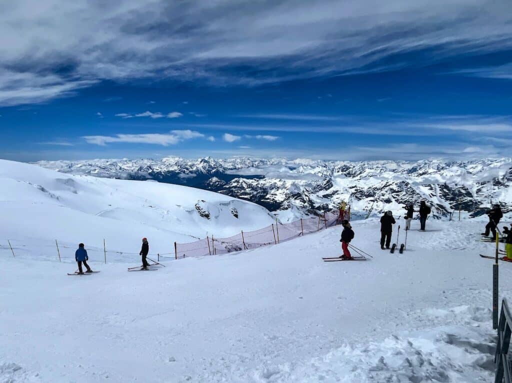 Skiers enjoy the thrilling slopes of Matterhorn Glacier Paradise, surrounded by an expansive snowy landscape and breathtaking mountain views. The vibrant blue sky and majestic peaks provide a stunning backdrop for winter sports enthusiasts carving through the fresh powder.