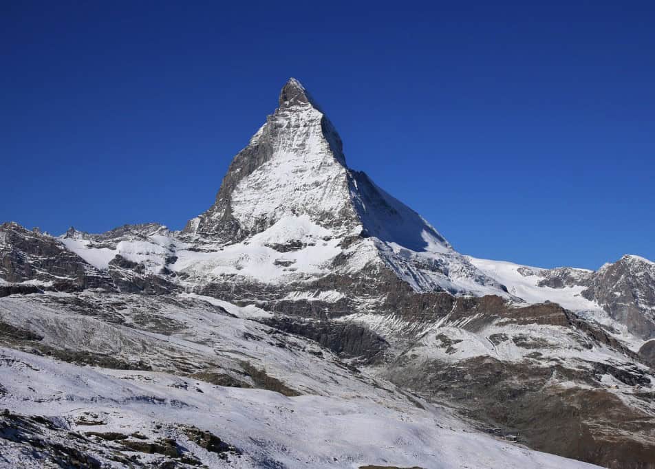 Breathtaking view of the Matterhorn from Riffelberg, showcasing the snow-capped mountain against a vibrant blue sky with rocky terrain in the foreground.