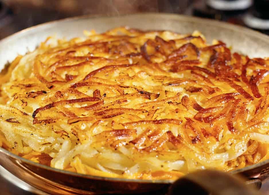 A delicious plate of Rösti, a Swiss specialty made from crispy fried potatoes, presented in a rustic pan and garnished with fresh herbs.