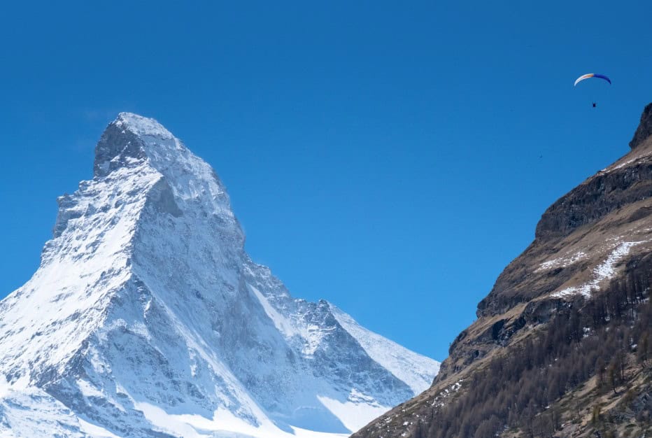 A paraglider floats above alpine slopes with the snow-covered Matterhorn rising behind. This is one of the best things to do in Zermatt in summer if you're up for a thrilling view from the sky.