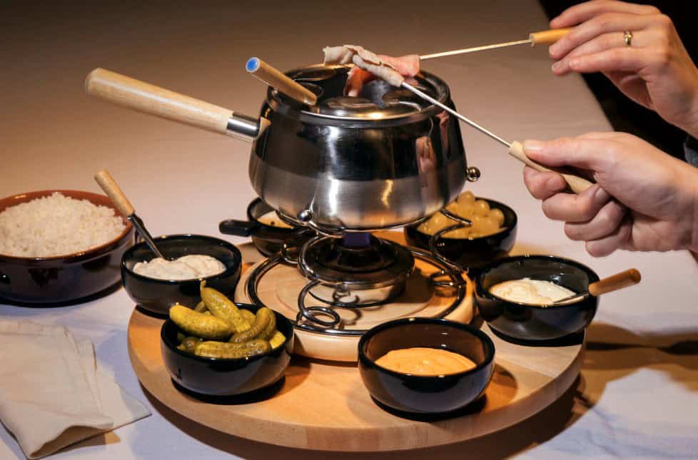 A traditional meat fondue setup in Zermatt with thinly sliced meats served alongside tangy pickles and a variety of flavorful dipping sauces for a savory experience.